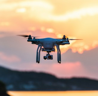 Drones hovering above a crop field during sunset.