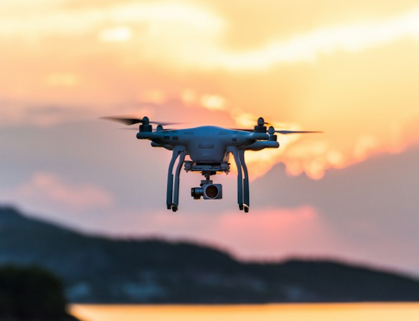 Drones hovering above a crop field during sunset.